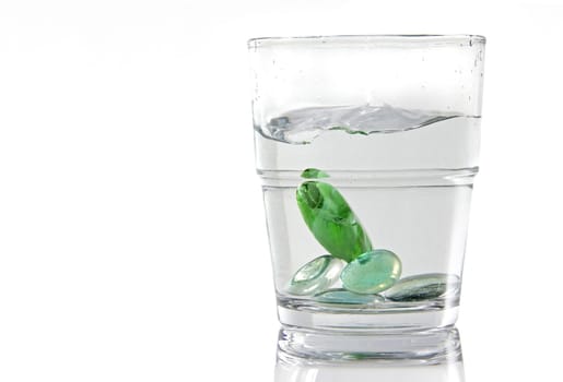 Marbles being dropped in a glass of water. White background isolated image