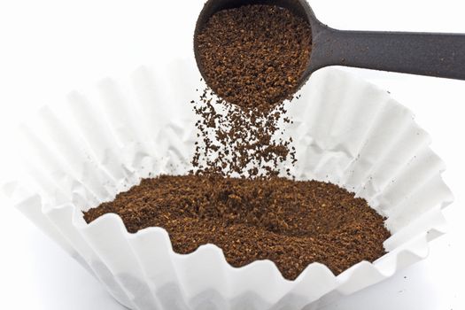 Pouring ground coffee into a paper filter with a plastic scoop