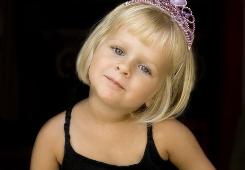 A 4 year old  blond little girl with a pink tiara. Isolated on black
