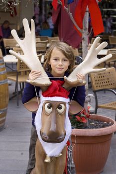 A girl sitting on a funny statue of a reindeer wearing a christmas hat