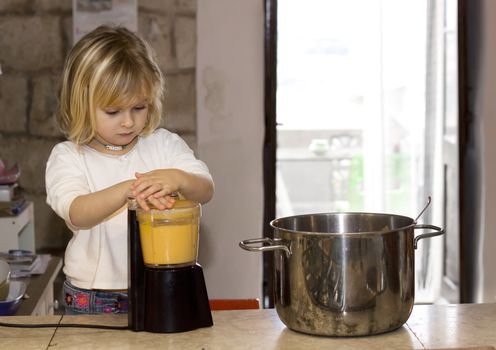 A young 4 year old girl is blending soup in a countryhouse farm kitchen, helping mummy to cook