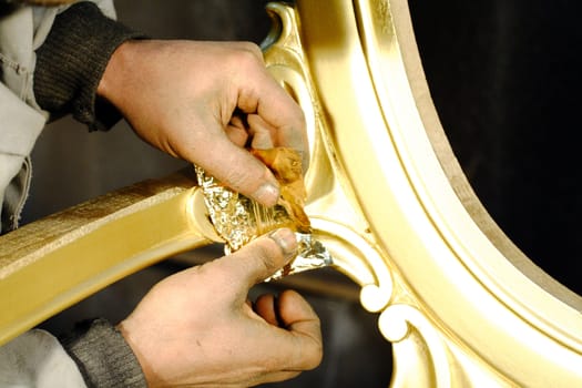 Art worker gliding a part of a chair with gold film