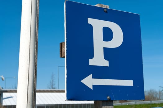 Parking sign with a white 'P' on a blue metal plate with clear blue sky background horizontal