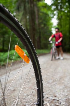 Mountain biking in a forest - bikers on a forest biking trail (shallow DOF, focus on the bike wheel in the foreground)