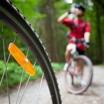 Mountain biking in a forest - bikers on a forest biking trail (shallow DOF, focus on the bike wheel in the foreground)