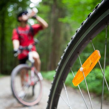 Mountain biking in a forest - bikers on a forest biking trail (shallow DOF, focus on the bike wheel in the foreground)