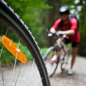 Mountain biking in a forest - bikers on a forest biking trail (shallow DOF, focus on the bike wheel in the foreground)