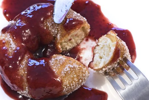 A cinnamon donut smothered in a rasberry puree sauce being eaten with fork and knife.