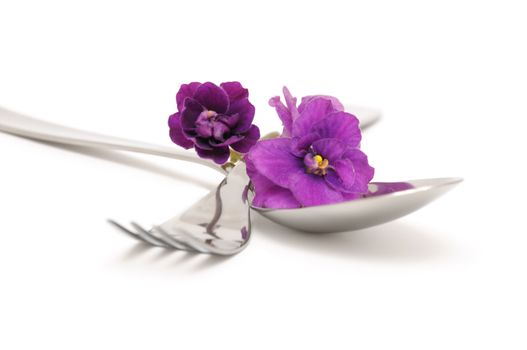Spoon and fork with violets on a white background closeup