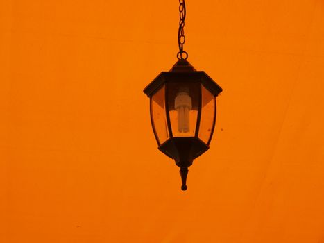 Old style lamp hanging on chain on bright yellow background
