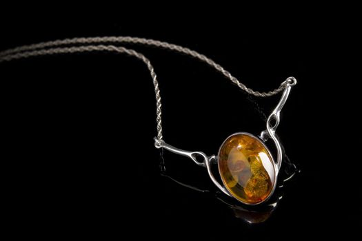 an oval amber stone set in a silver pendant with attached silver link chain on shiny black background