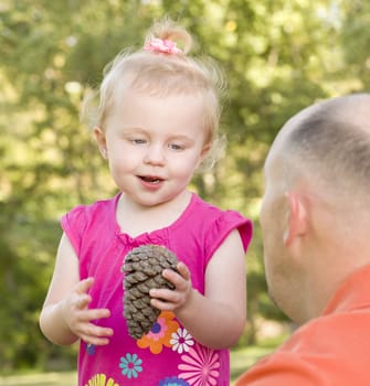 Adorable Young Girl Holding Pine Cone Talks to Her Dad in The Park.