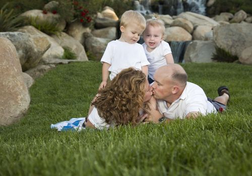 Affectionate Couple Kiss as Adorable Twins Watch in the Park.