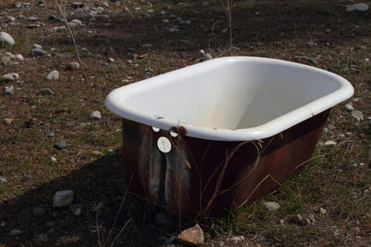 Rusted bath lying in a grass and rock field