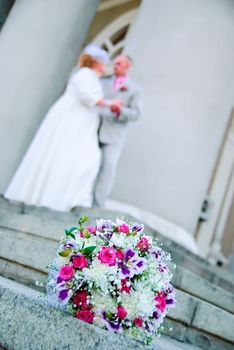 Bridal bouquet on the stone stairs and blurred newlyweds