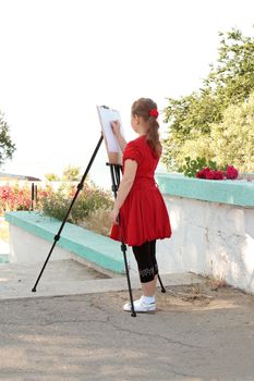 Girl draws pencil behind his easel painting. Isolated on white background.