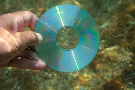 CD in hand under the water. Close-up.
