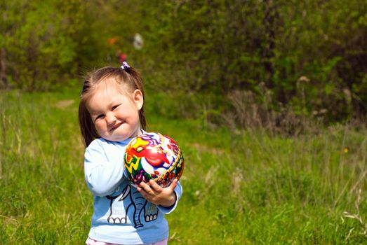 Little girl with the ball in hands on the meadow