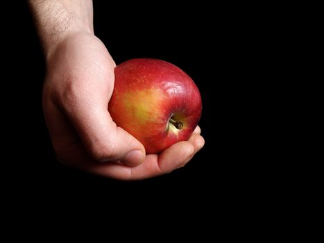 Men's hand photographed holding an apple. With a black background.