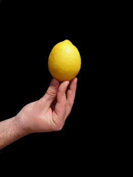 Men's hand holding lemon upwards.