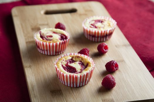 Three raspberry cheesecake muffins with fresh raspberries.