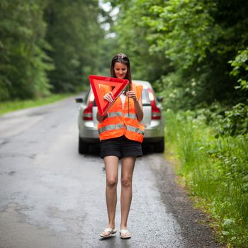 Young female driver wearing a high visibility vest, calling the roadside service/assistance after her car has broken down