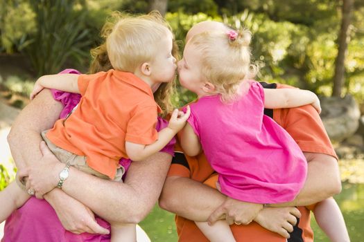 Mom and Dad Holding Kissing Brother and Sister Toddlers in the Park.