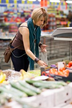 Beautiful young woman shopping for fruits and vegetables in produce department of a grocery store/supermarket