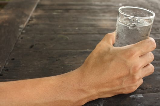 Man hand holding a glass of water on wood background