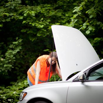 Young female driver wearing a high visibility vest, calling the roadside service/assistance after her car has broken down