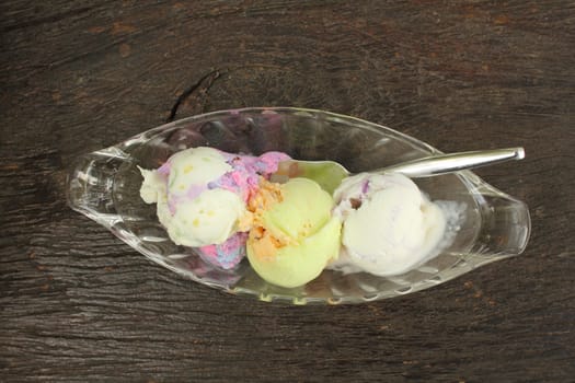 Three scoop of ice cream in glass plate on wood background