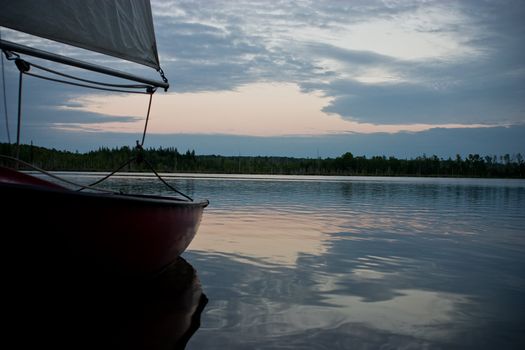 Tiny red sailboat sitting peacefully on the lake at sunset
