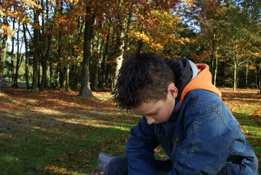 Sad young boy sitting in the park.