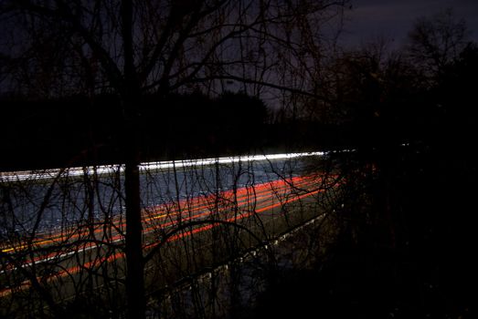 A nighttime highway shot using slow shutterspeed - glowing light trails are visible through the trees.