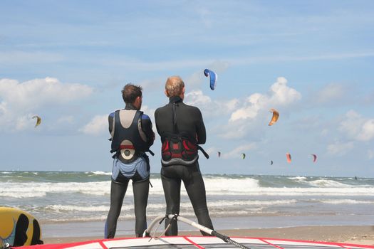 Two surfers watching kitesurfers in action