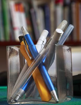 Image of different writing tools in a glass support on an office table.