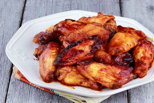 Plate of delicious barbecue chicken wings with shallow depth of field on a rustic background.