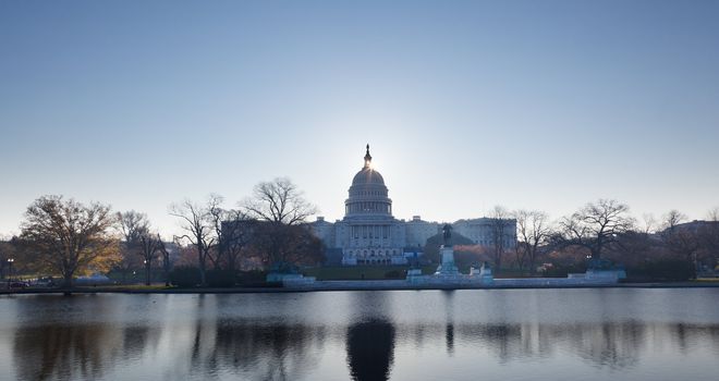 Brightly lit dawn sky behind the illuminated dome of the Capitol in Washington DC with the pool and statues