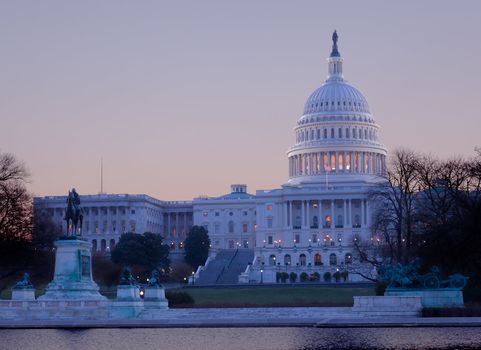 Brightly lit dawn sky behind the illuminated dome of the Capitol in Washington DC with the pool and statues