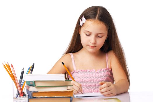 Cute little girl writing something in the copybook with pencils and books near it.