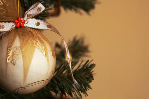  White Christmas ornament with ribbon hanging on a pine tree branch. 
