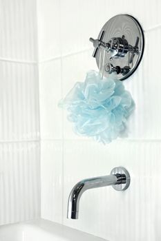 Modern renovated bathroom with corrugated glossy white tiles around the shower tub stall, chrome faucet and blue puff.