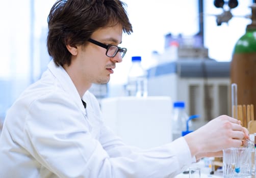 young, male researcher/chemistry student carrying out scientific research in a lab (shallow DOF; color toned image)