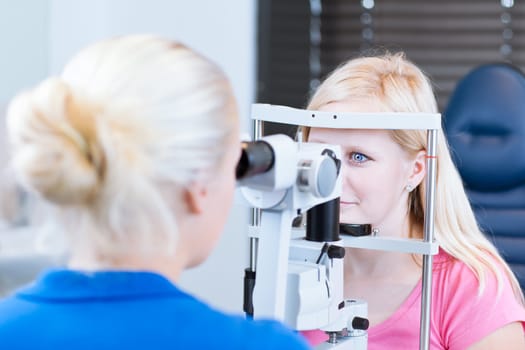 optometry concept - pretty, young female patient having her eyes examined by an eye doctor (color toned image; shallow DOF)