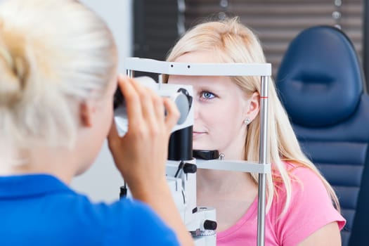 optometry concept - pretty, young female patient having her eyes examined by an eye doctor (color toned image; shallow DOF)