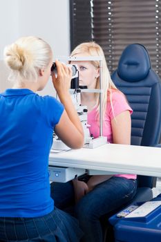 optometry concept - pretty, young female patient having her eyes examined by an eye doctor (color toned image; shallow DOF)