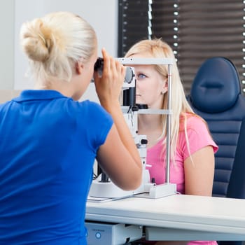 optometry concept - pretty, young female patient having her eyes examined by an eye doctor (color toned image; shallow DOF)