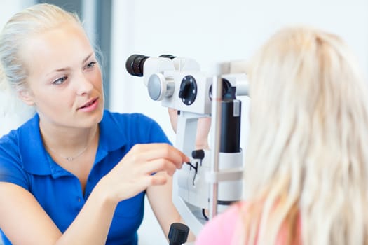 optometry concept - pretty, young female patient having her eyes examined by an eye doctor (color toned image; shallow DOF)