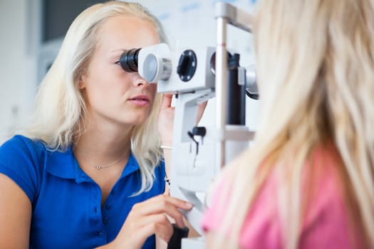 optometry concept - pretty, young female patient having her eyes examined by an eye doctor (color toned image; shallow DOF)