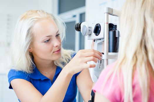 optometry concept - pretty, young female patient having her eyes examined by an eye doctor (color toned image; shallow DOF)